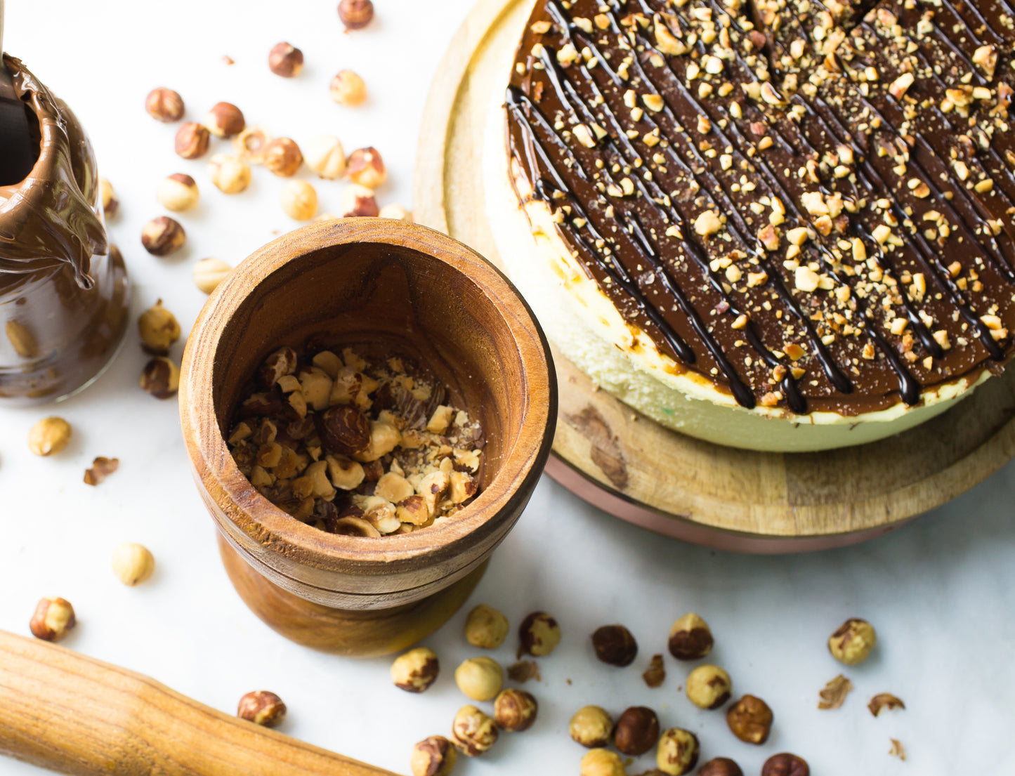 overhead image of nutella cheesecake with hazelnuts and chocolate on top by la roma pastry shop in oakdale new york with more hazelnuts scattered around and pieces in wooden mortar with pestle laying nearby