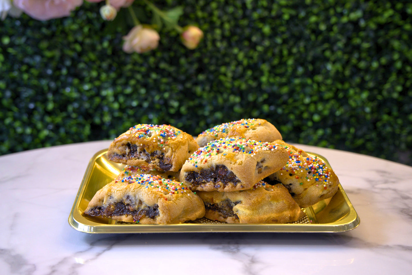 A display of Cuccidati in front of floral greenery from La Roma Pastry Shop