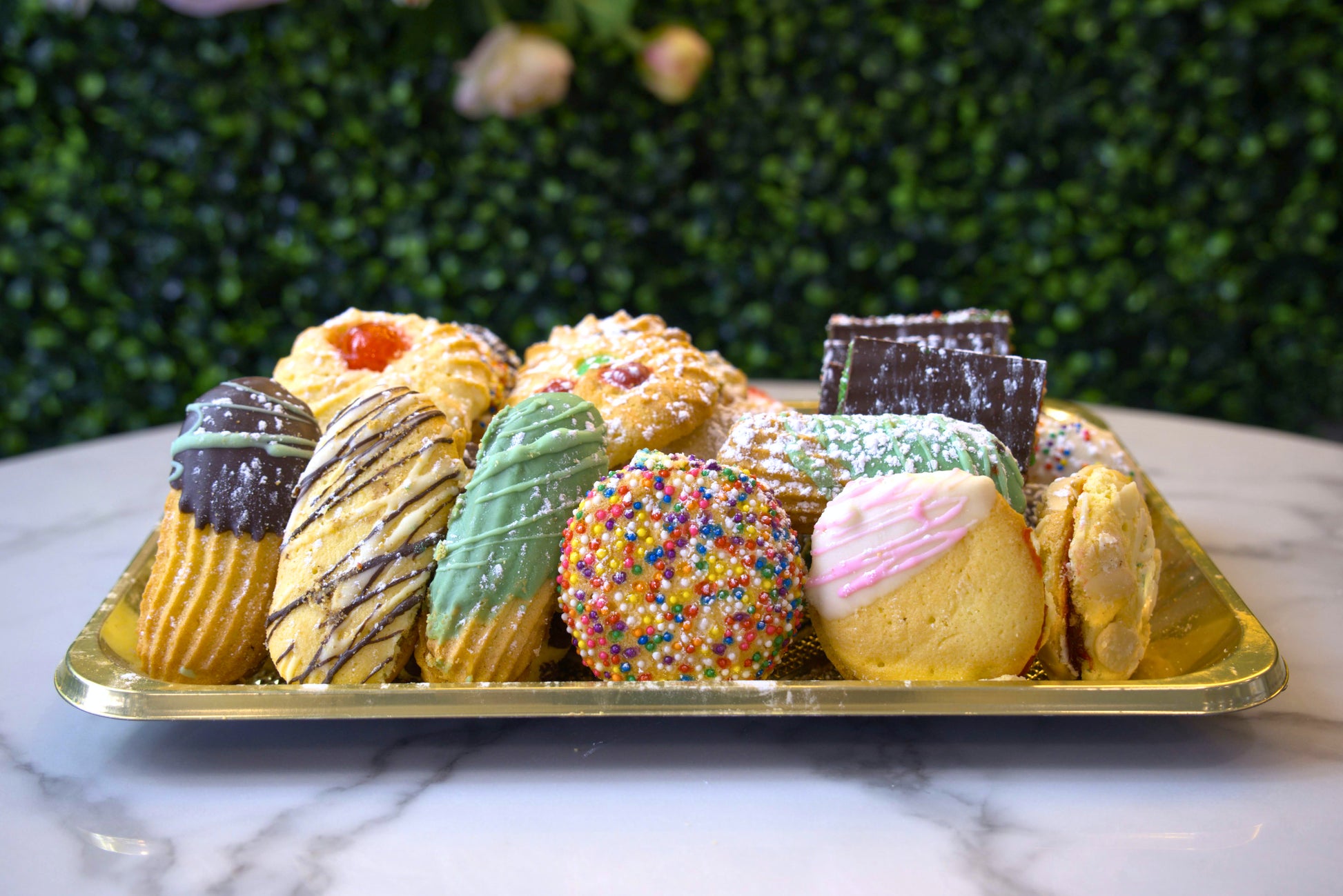 A tray of assorted butter cookies in front of greenery from La Roma Pastry Shop