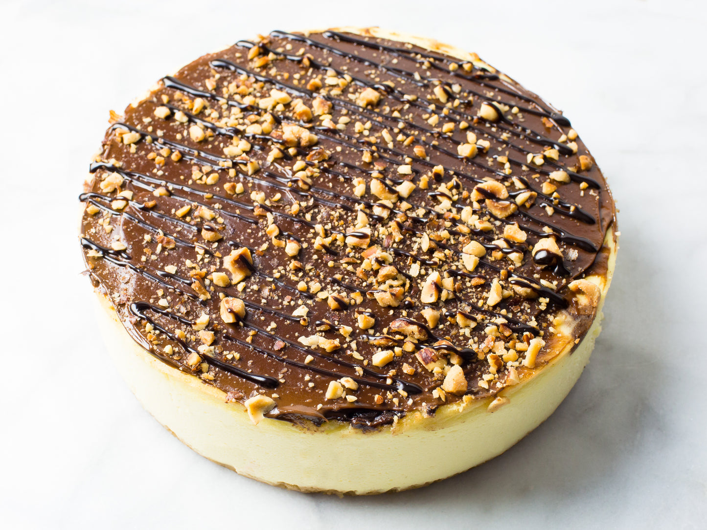 close up image of nutella cheesecake made by la roma pastry shop in new york with chopped hazelnuts on top and chocolate drizzle