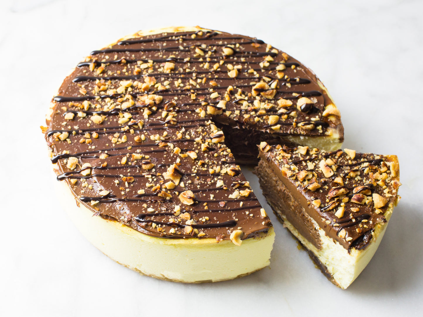 nutella cheesecake with chopped hazelnuts and chocolate drizzle with slice cut out to reveal nutella center made by la roma pastry shop on long island new york