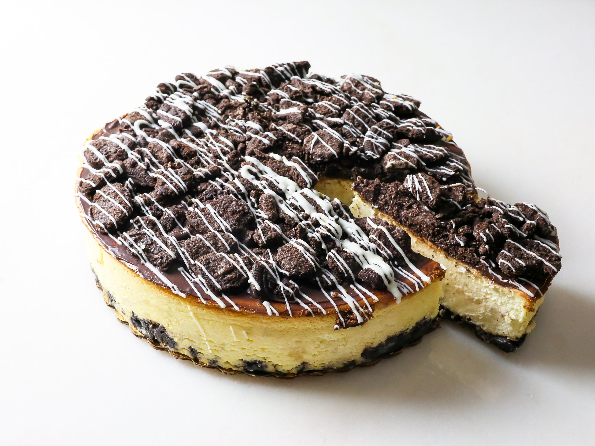 decadent oreo cheesecake made by la roma pastry shop on long island new york with frosted drizzle glazing the top and slice taken out