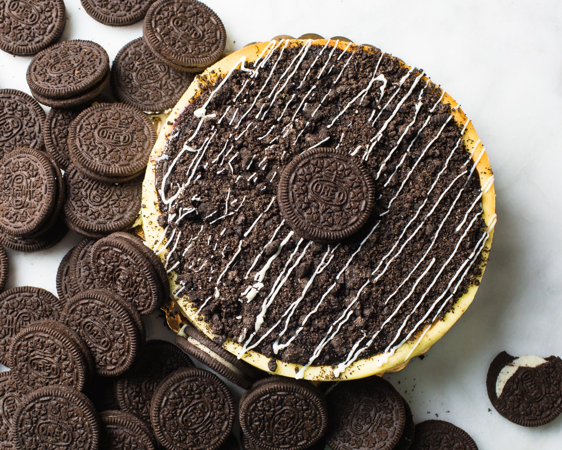 overhead shot of oreo cheesecake made by la roma pastry shop in oakdale new york with oreos scattered around and crumbled cookies with frosted drizzle on top
