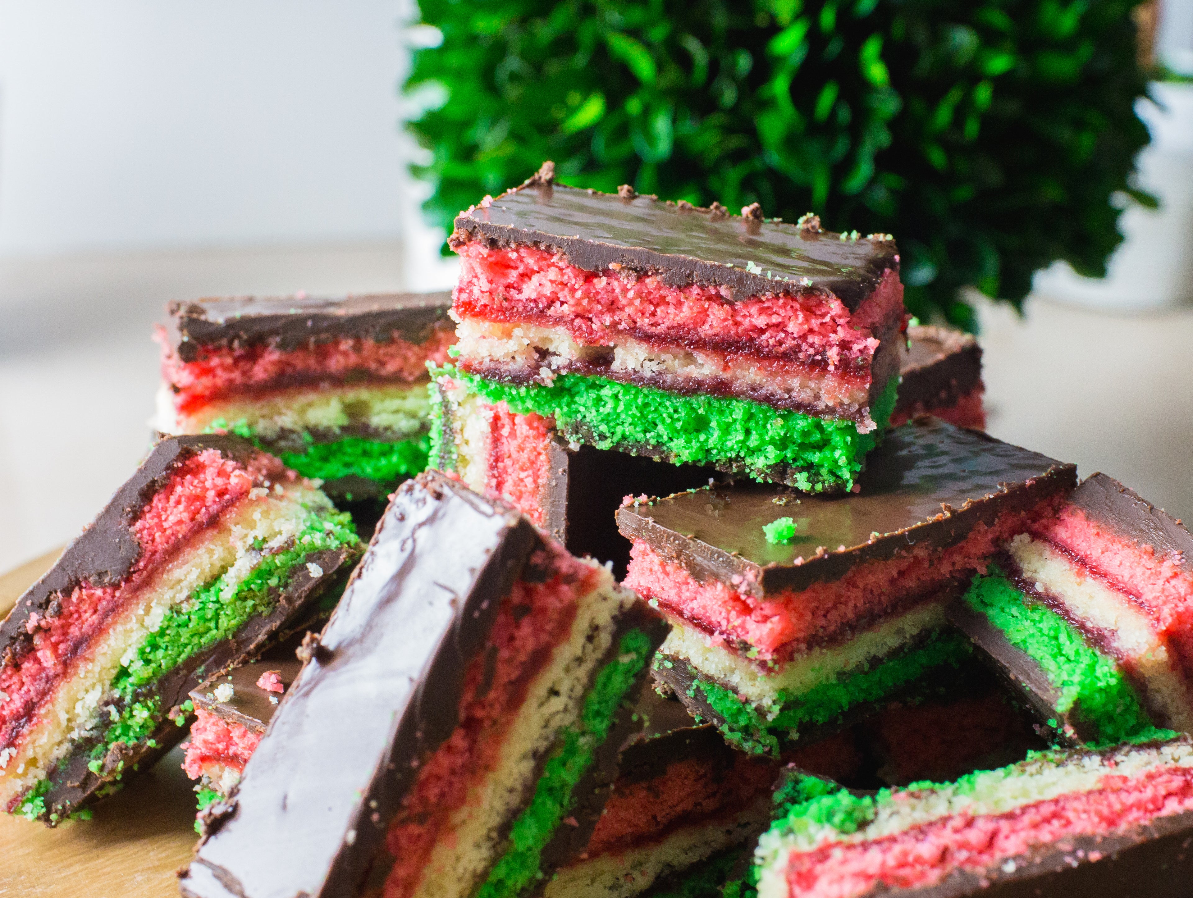 close up image of rainbow cookies from la roma pastry shop on long island which feature red white and green cake with berry filling and chocolate 