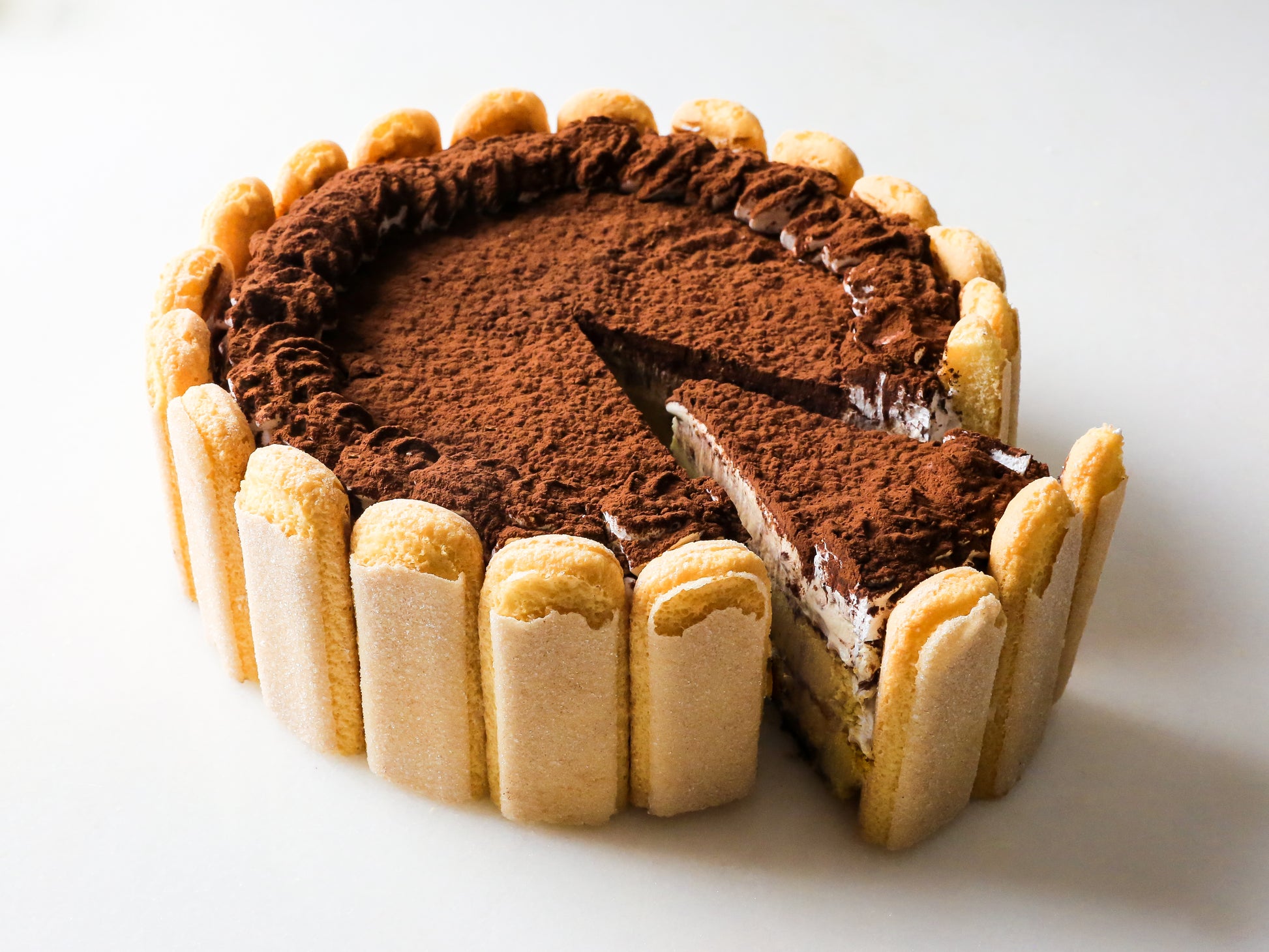 tiramisu cheesecake with a slice taken out and lady finger cookies around the edge made on long island new york by la roma pastry shop
